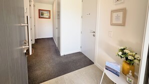 A hallway with a carpeted floor, a white door with a privacy sign, a framed picture on the wall, and a small table with a vase of flowers and a bottle. - Modern private suite on local cherry orchard (Cromwell)