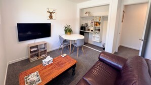 A living room with a TV, a coffee table, a couch, and a dining area with a table and chairs. - Modern private suite on local cherry orchard (Cromwell)
