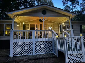 A covered porch with a white lattice railing, a staircase leading up to a deck, and a small porch area with a bench.