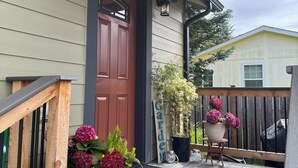 Um deck de madeira com uma porta vermelha, plantas em vasos e uma placa com a inscrição 'Garden'.