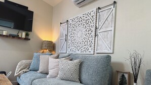 Sala de estar com sofá cinza, arte decorativa na parede, televisão de tela plana e um abajur.