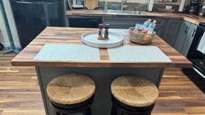 Uma ilha de cozinha com dois bancos, almofada de assento trançada, uma pequena mesa redonda e uma cesta com garrafas de água.