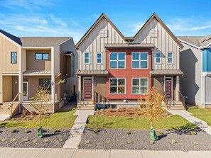 A row of modern townhouses with a central red door, a covered front porch, and a well-maintained lawn. - Spacious 3BR Retreat | Sleeps 8 | 15 Min Airport (Calgary)