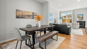 A modern living room with a dining area, featuring a large painting, a vase with flowers, and a sofa. - Spacious 3BR Retreat | Sleeps 8 | 15 Min Airport (Calgary)