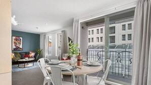 A modern dining area with a round table set for four, white chairs, and a view of a cityscape through large windows. - Perfect City Retreat 1 bdrm Prime Location (Christchurch)