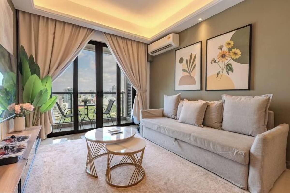 A modern living room with a sofa, two round tables, a large window with curtains, and two wall-mounted air conditioning units.