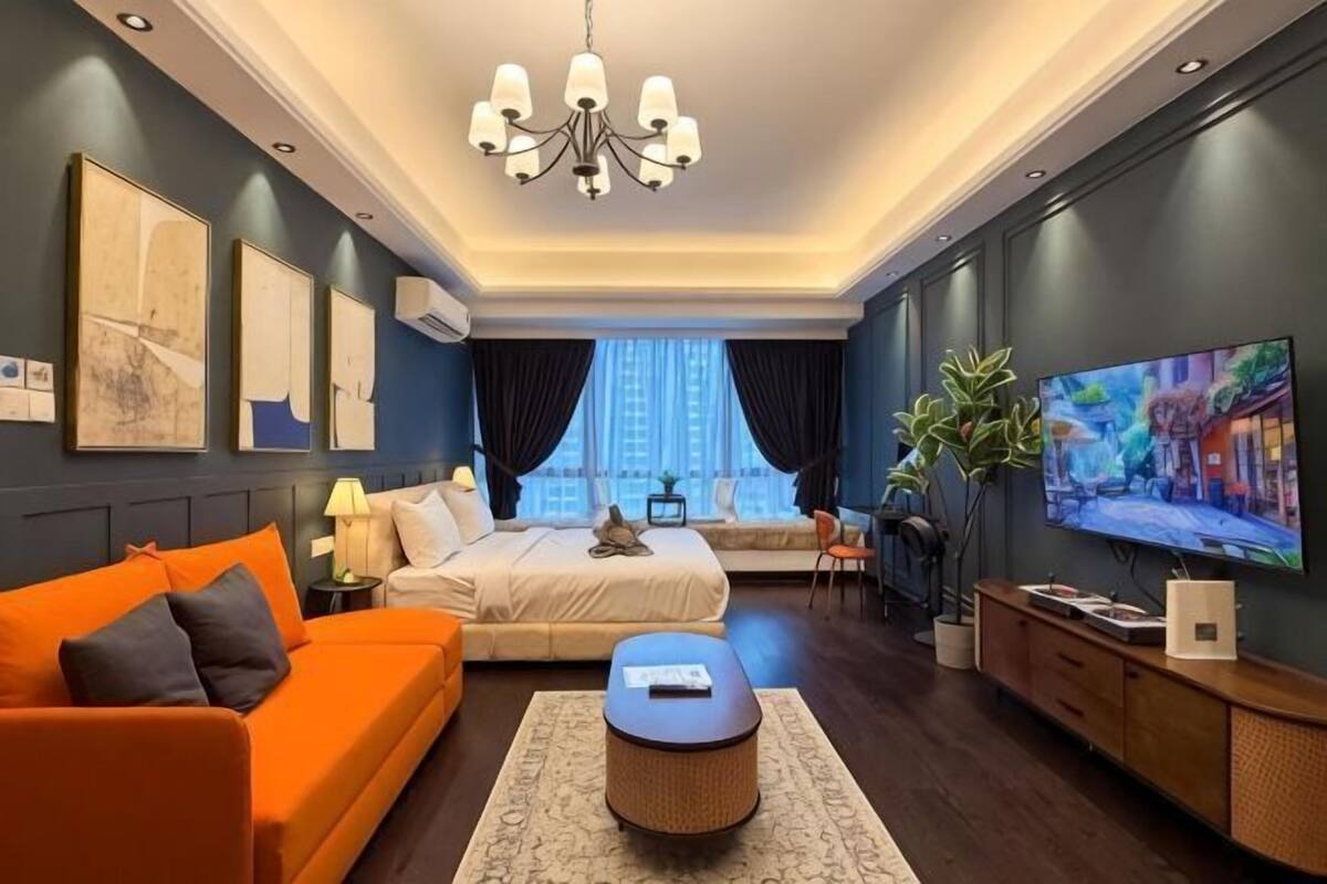 A modern hotel room with a bed, orange sofa, television, and a large window.