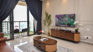 A modern living room with a large TV, a sofa, a coffee table, and a view of the outdoors. - R&F Princess Cove by Nest Home at Johor Bahru (Johor Bahru)