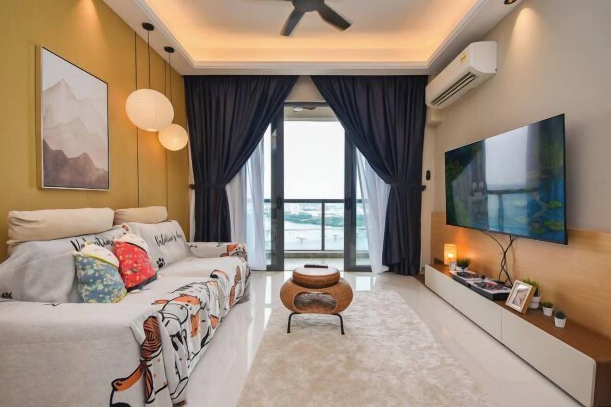 A modern living room with a sofa, a coffee table, a TV mounted on the wall, and a large window with curtains.