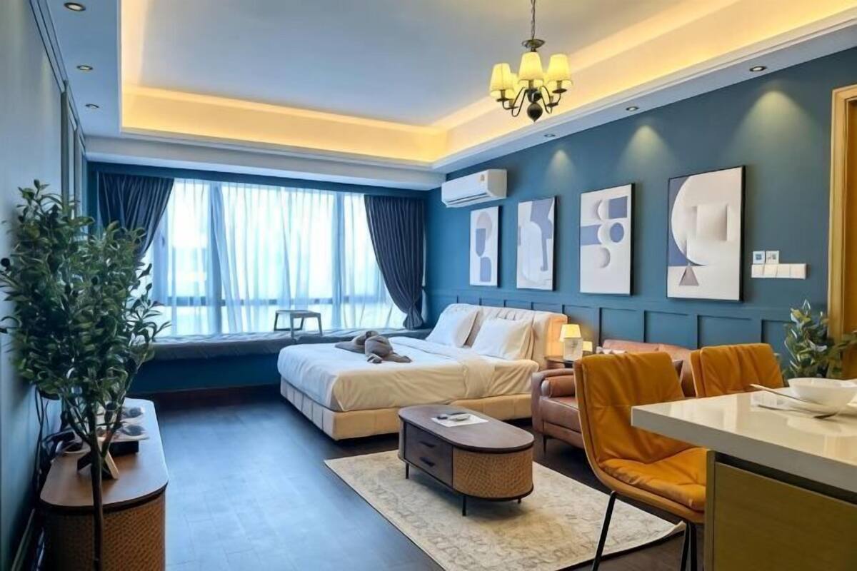 A hotel room with a bed, a desk, a chair, a potted plant, and artwork on the walls.