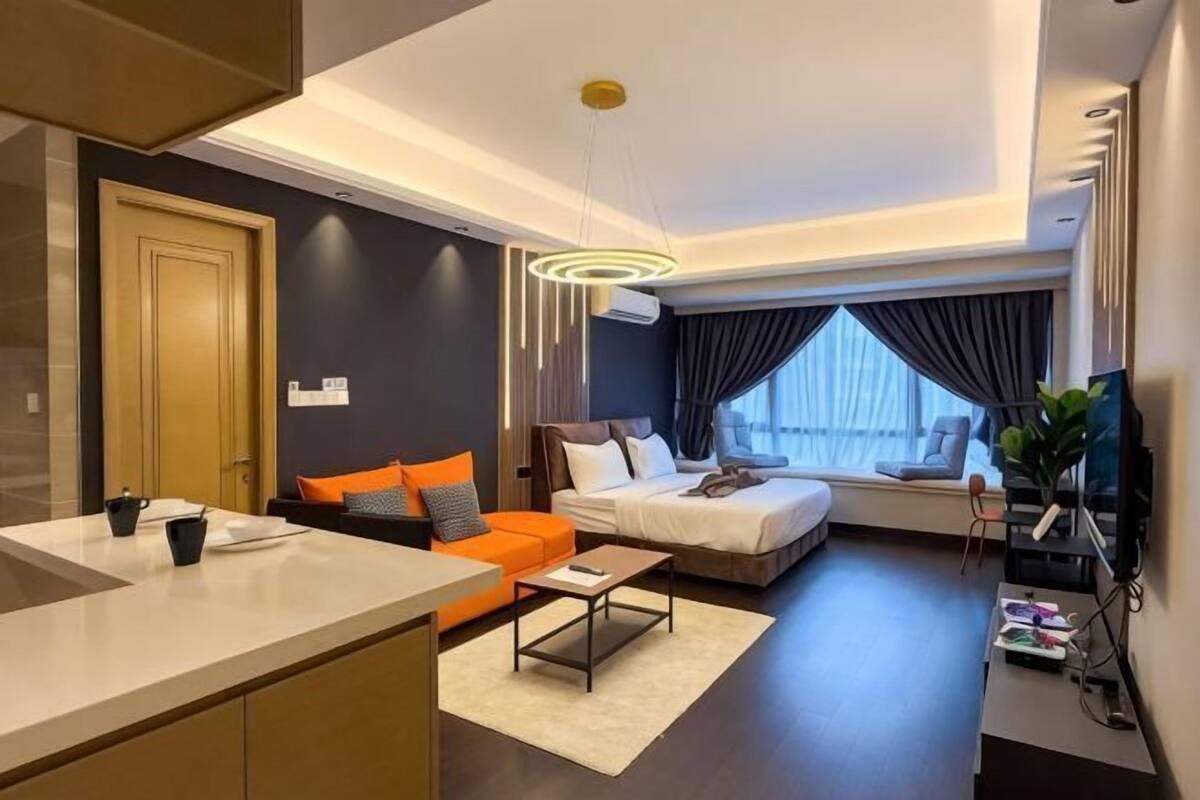 A modern hotel room with a kitchenette, a sofa, a bed, and a large window.