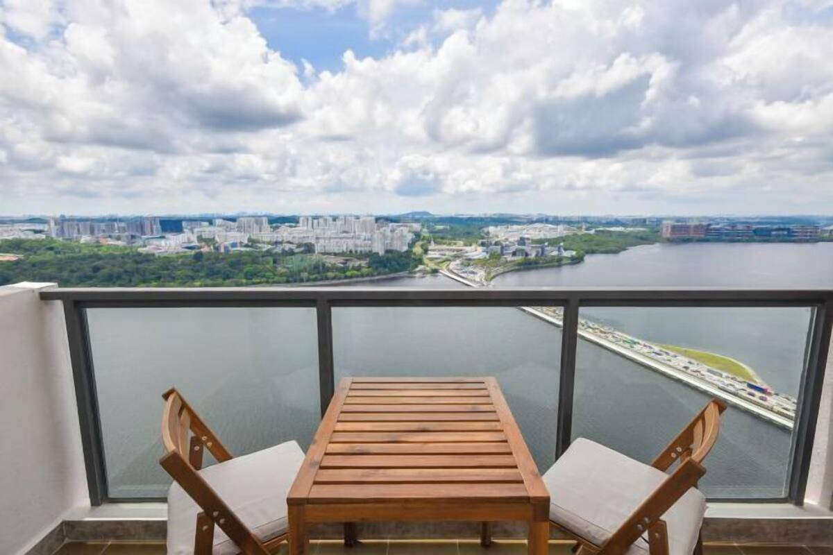 A balcony with a wooden table and chairs, overlooking a cityscape and a body of water.