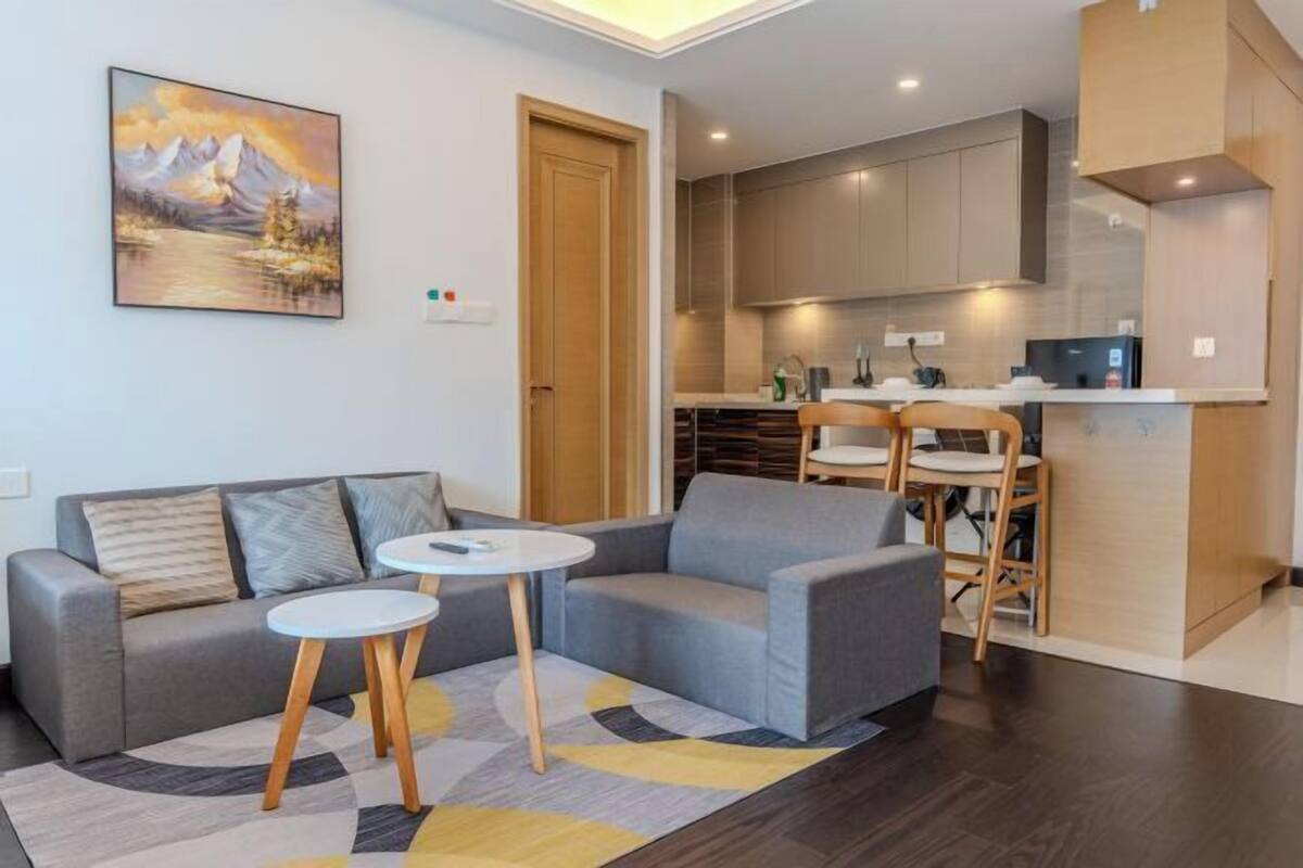 A modern living room with a sofa, a small round table, and a kitchen area with cabinets and a countertop.