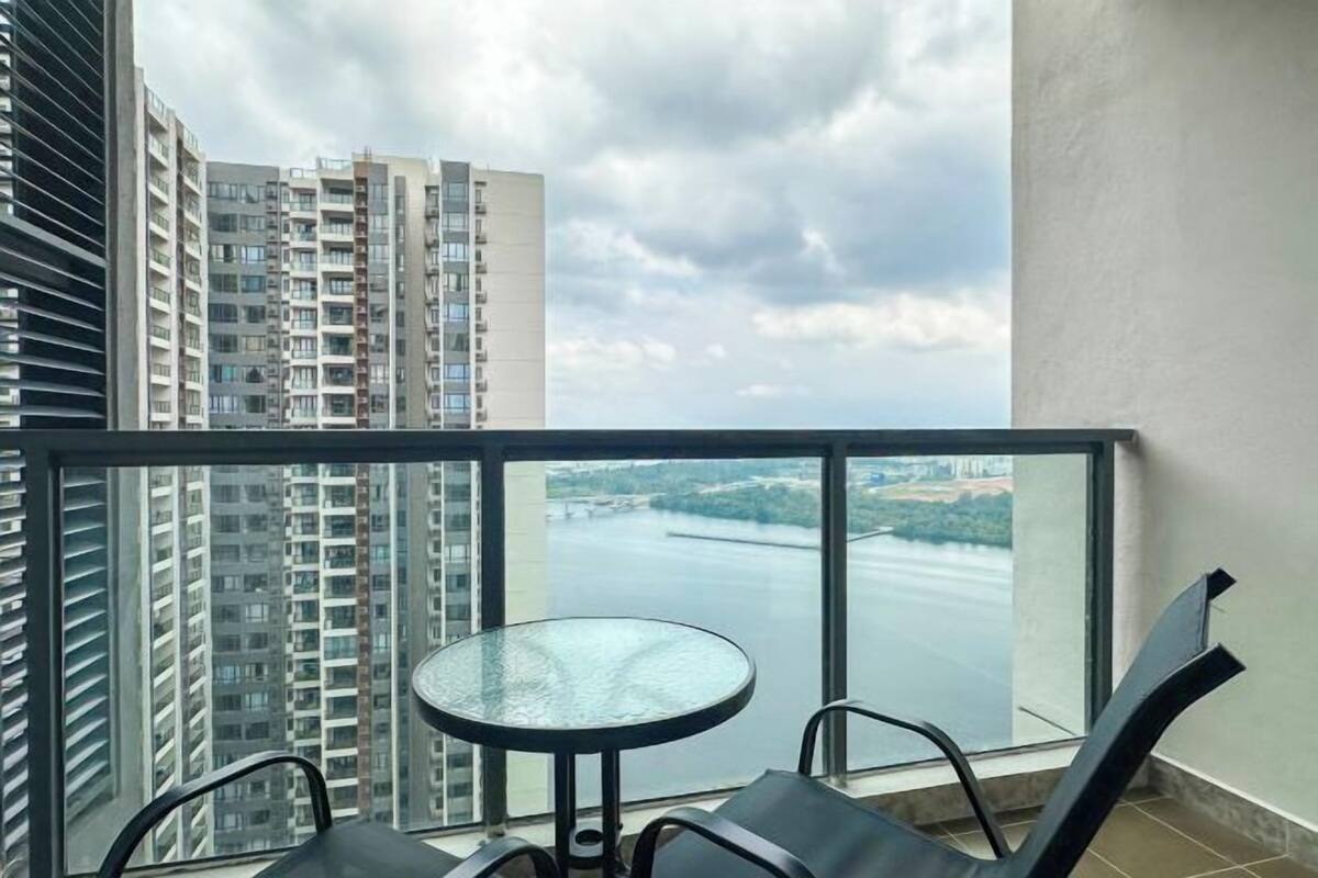 A balcony with a glass table and chairs, overlooking a river and high-rise buildings.