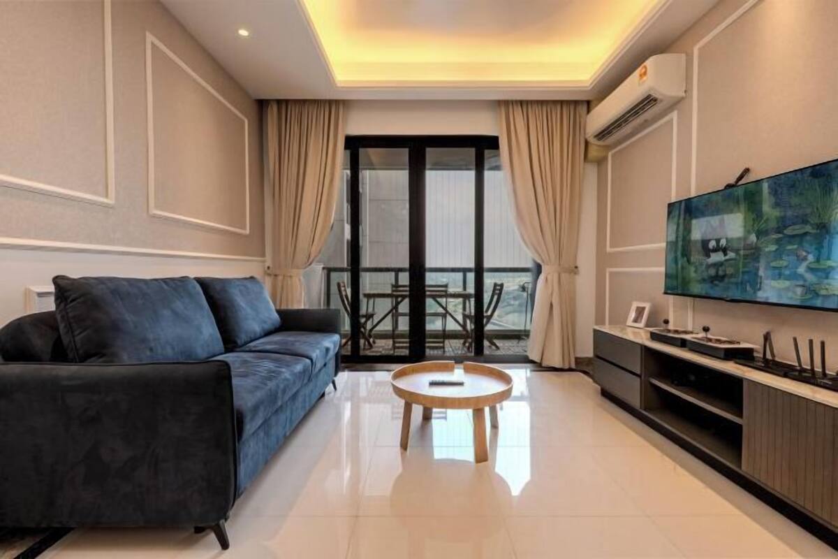 A modern living room with a sofa, a coffee table, a TV, and a balcony with curtains.