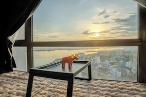 A room with a large window overlooking a cityscape, a small table with a toy moose, and a textured rug.
