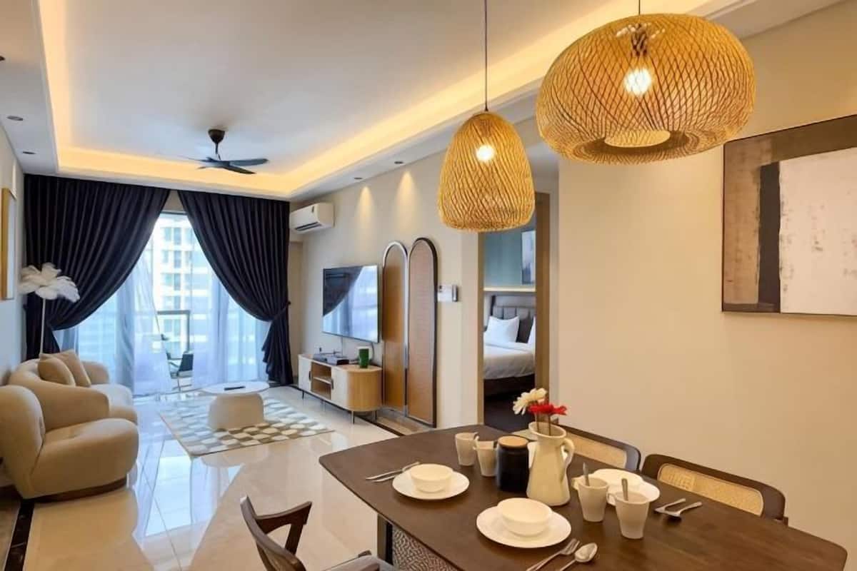 A modern hotel room with a dining area, a sofa, a TV, and a kitchen area.