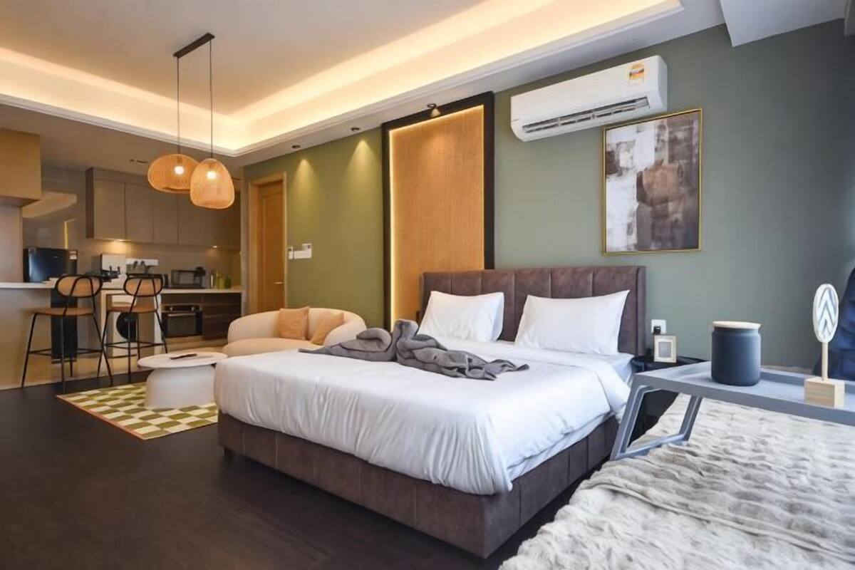 A modern hotel room with a large bed, a desk, and a kitchenette.