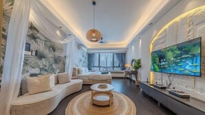 A modern living room with a curved sofa, a round coffee table, a flat-screen TV, and a large painting. - R&F Princess Cove by Nest Home at Johor Bahru (Johor Bahru)