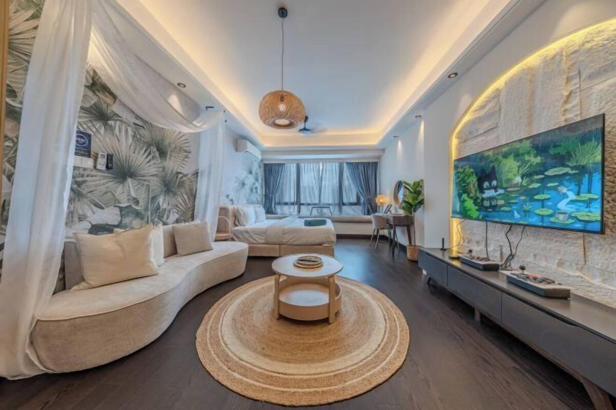 A modern living room with a curved sofa, a round coffee table, a flat-screen TV, and a large painting.