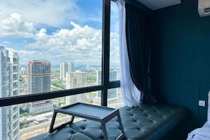 A room with a view of city buildings, a window with curtains, and a small table.