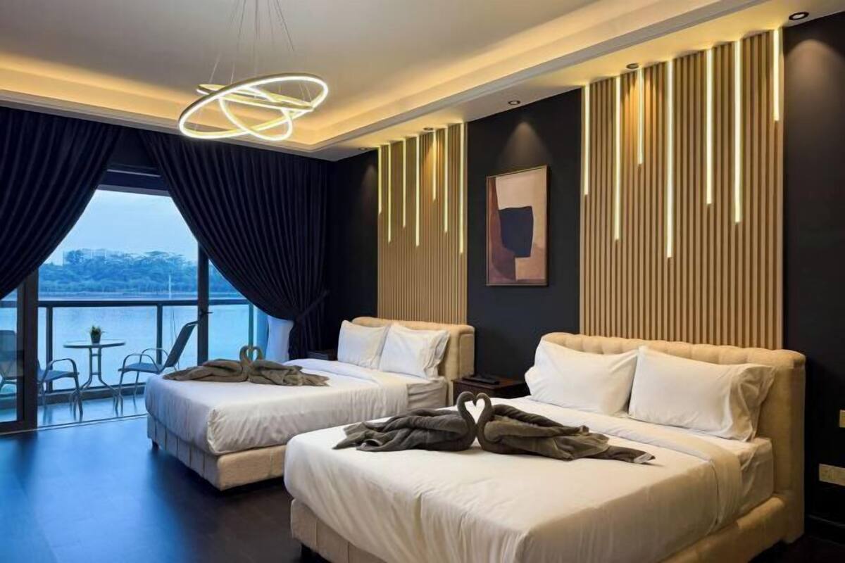 A hotel room with two beds, a large window with curtains, a view of the water, and a modern light fixture.