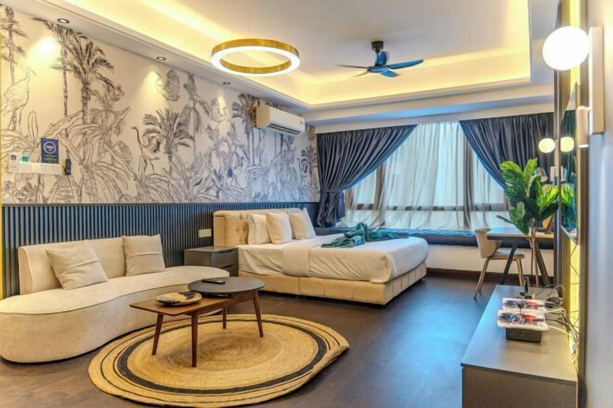 A modern hotel room with a sofa, a bed, a small table, and a large window with curtains.