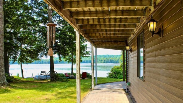 A covered porch with a view of a lake, wooden walls, and a hanging wind chime. - SR/SL Two Lakefront Homes w/Sauna, Decks, Sleeps 16 – Perfect for Families (Toivola)