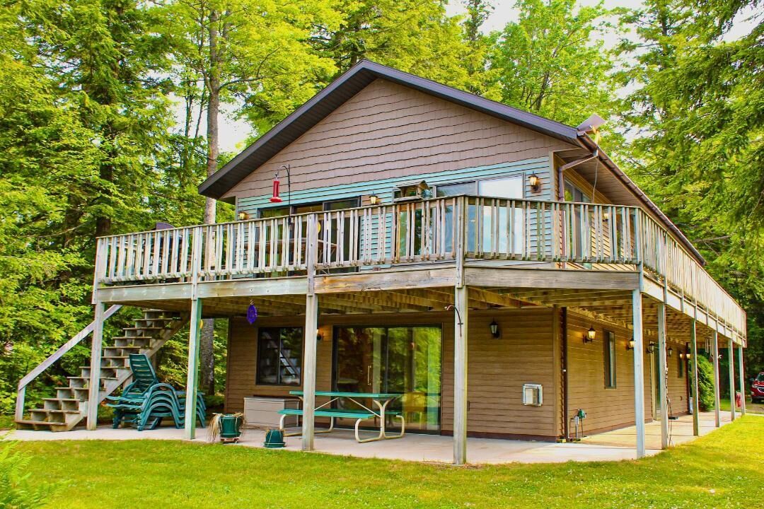 Un chalet à deux étages doté d’un balcon, d’un espace salon extérieur et d’un escalier menant à une terrasse.