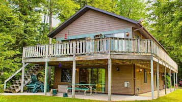 Un chalet à deux étages doté d’un balcon, d’un espace salon extérieur et d’un escalier menant à une terrasse.