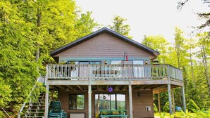 A two-story cabin with a balcony, surrounded by lush greenery. - SR/SL Two Lakefront Homes w/Sauna, Decks, Sleeps 16 – Perfect for Families (Toivola)