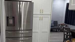 A modern kitchen with white cabinetry, a stainless steel refrigerator, and a marble countertop.