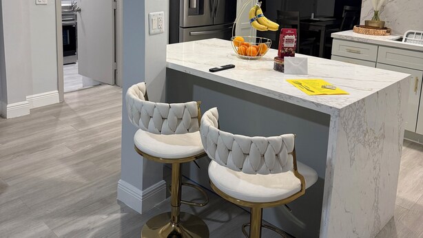 A modern kitchen with white cabinets, stainless steel appliances, and a marble island with two bar stools.