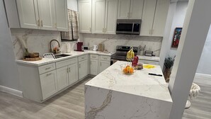 A modern kitchen with white cabinetry, a marble island, and a stainless steel oven.