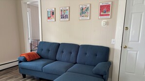 Un sofá seccional azul con una manta naranja, un tapete estampado y tres cuadros en la pared.
