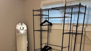 Un dormitorio con cama, una estantería metálica, un espejo y una ventana con persianas.