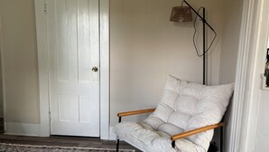 Una habitación con una puerta blanca, un sillón estampado, una lámpara de pie y una alfombra con diseño.