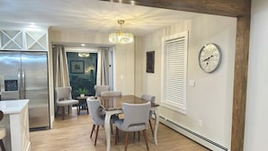 A modern kitchen with a stainless steel refrigerator, a dining area with a wooden table and grey chairs, and a chandelier. - Renovated 3-bedroom house in Montgomery VT, close to Jay Peak (Montgomery Center)