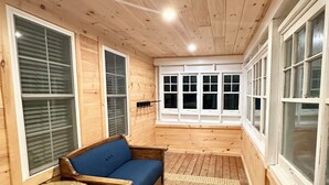 A wooden cabin interior with a blue sofa, a small round table, and a window with blinds. - Renovated 3-bedroom house in Montgomery VT, close to Jay Peak (Montgomery Center)