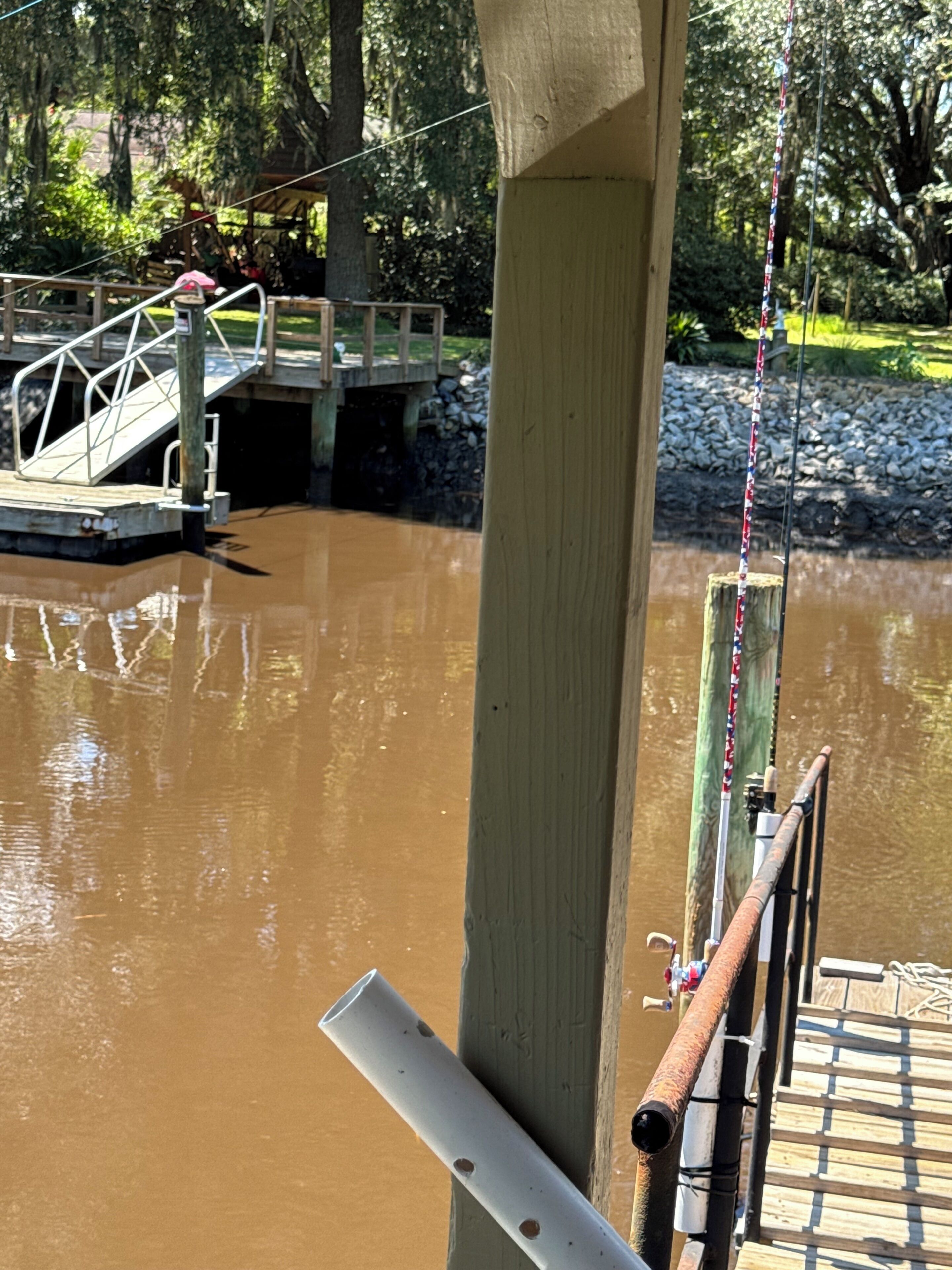 A wooden dock with a metal railing extending over a muddy water body.