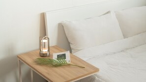 A neatly made bed with white bedding and pillows, a bedside table with a wooden finish, a lit lantern-style lamp, and a small plant on the table. - Yeosu Greenhouse Pension (Yeosu)