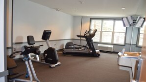 A fitness room with cardio equipment, including a stationary bike, elliptical, and treadmill, and a large window providing natural light. - Slopeside Ski-In/Out Condo 112 | Snowshoe Village (Snowshoe)