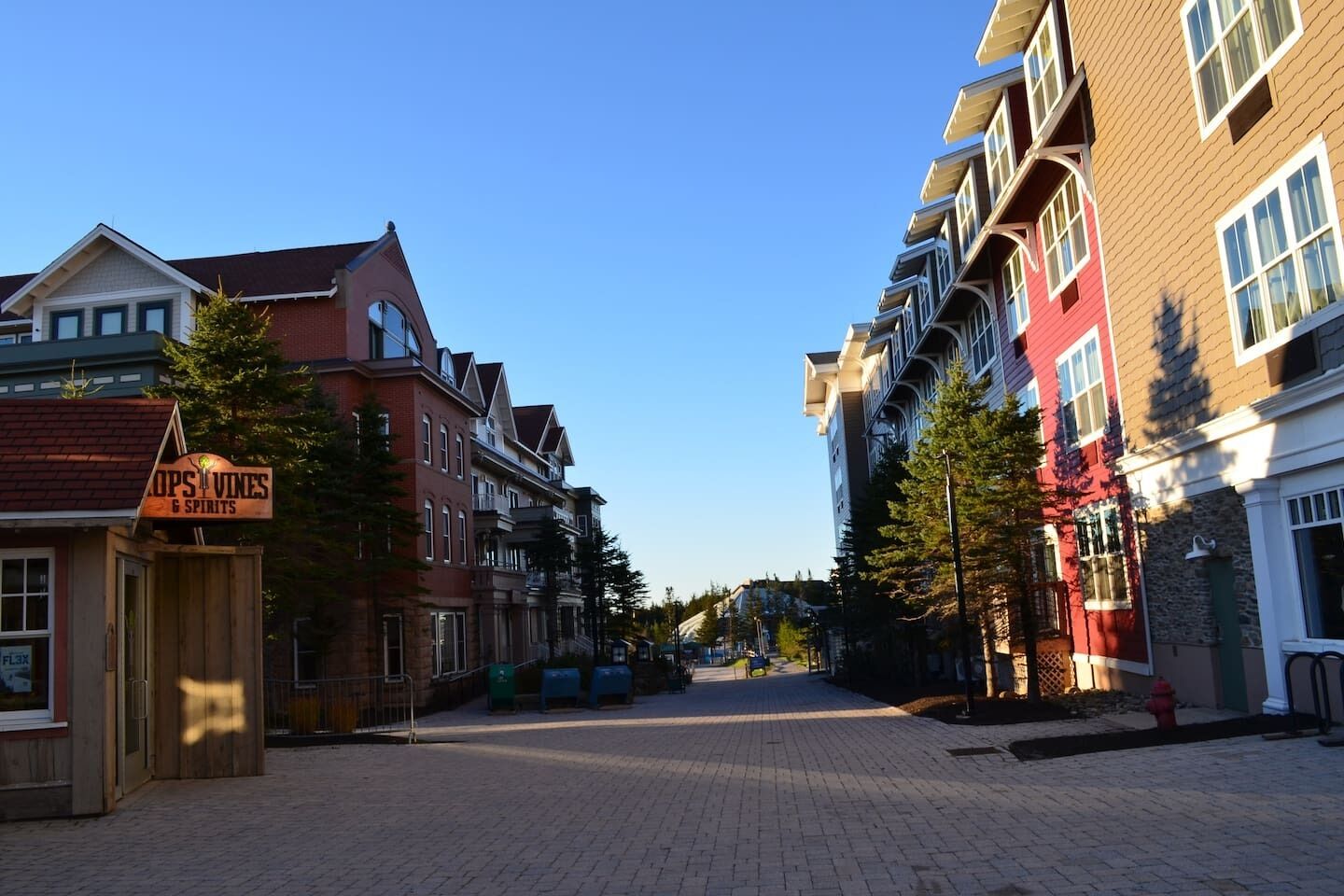 Een straat met meerhoogbouw, een bord voor 'OPSVINES & SPIRITS', en een helderblauwe lucht.