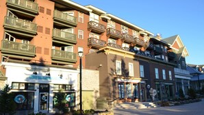 A multi-story building with balconies, a storefront with a sign, and a clear sky. - Slopeside Ski-In/Out Condo 112 | Snowshoe Village (Snowshoe)