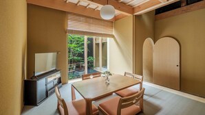 Een traditionele Japanse kamer met tatami vloeren, een lage tafel met kussens, een televisie en schuifdeuren die uitkomen op een tuin.