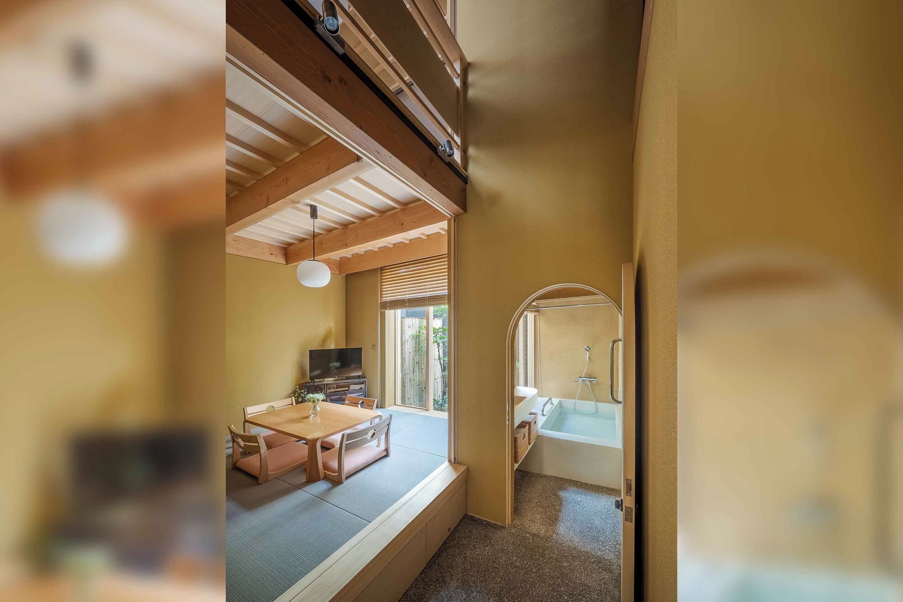 A room with a tatami mat seating area, a wooden ceiling, and a view of an outdoor space.