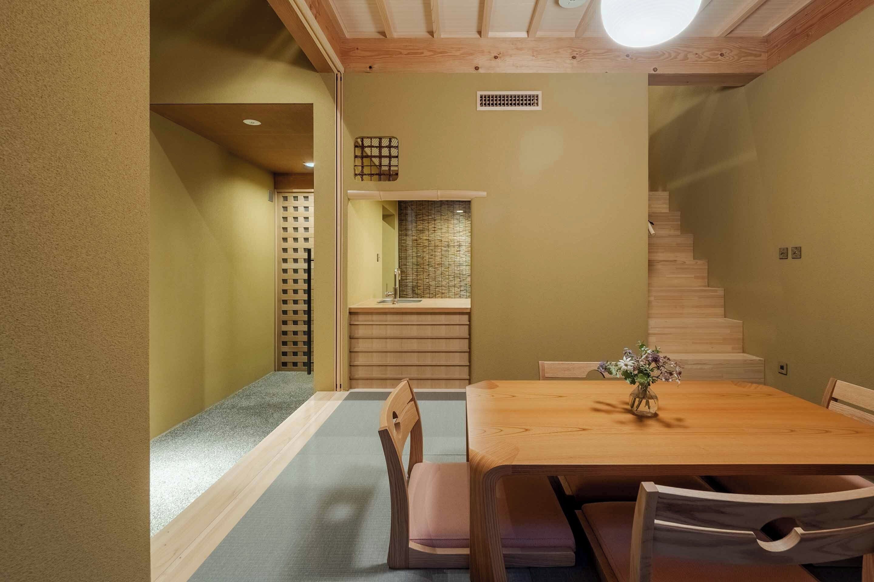 A dining area with a wooden table and chairs, a small vase with flowers, and a staircase leading to a loft space.