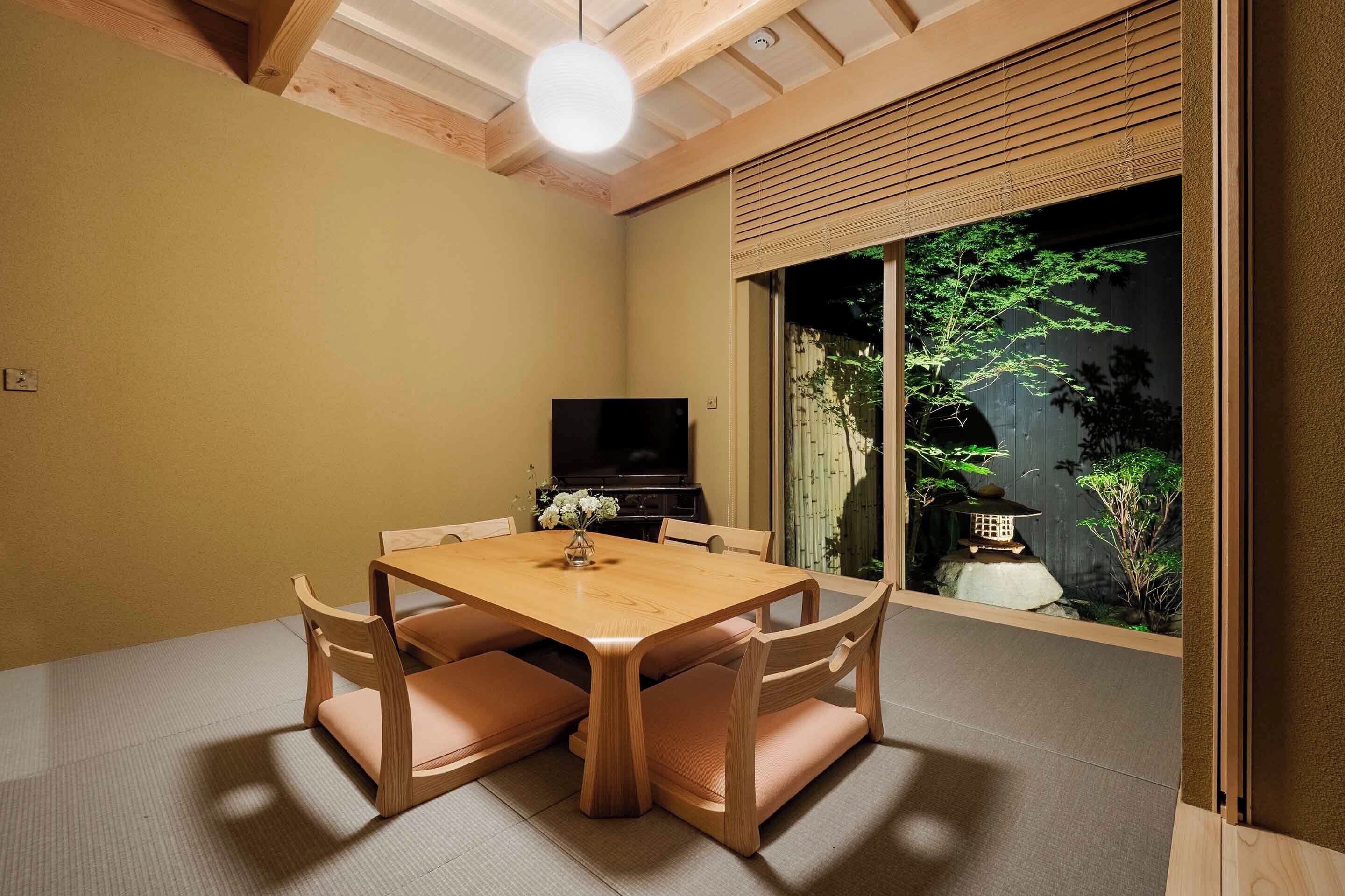 Un comedor con una mesa y sillas de madera, un televisor y vista a un jardín con un farol.