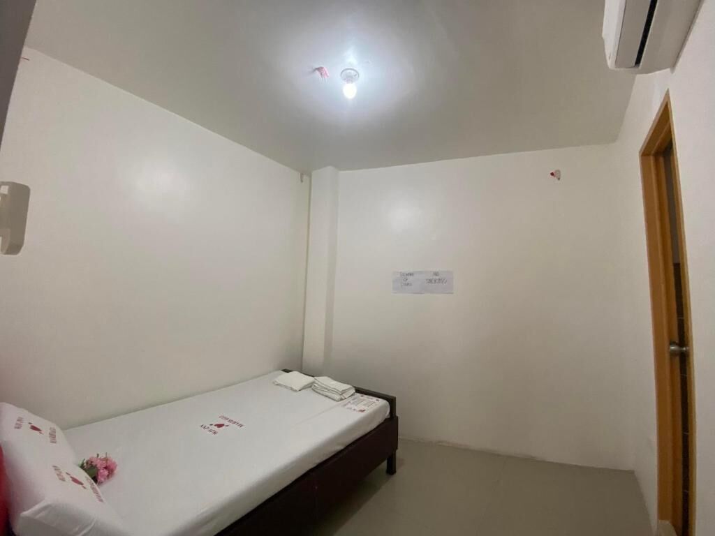 A small, clean room with a single bed, a ceiling light, and a door.