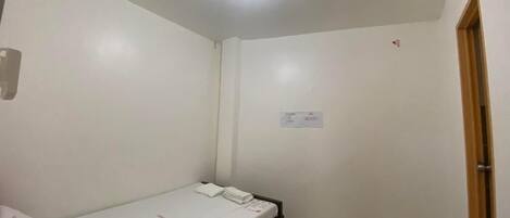 A small, clean room with a single bed, a ceiling light, and a door.